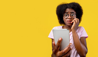 Scared african american woman holding mobile phone seeing bad news, photos or message and looking at camera over yellow background. Human reaction, expression