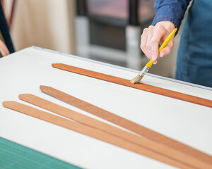 A craftsman uses a brush to cover leather parts. 