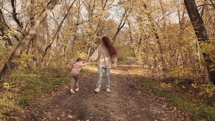 Fototapeta premium child runs around his mother and laughs in the park, happy family, cheerful child with mom plays a game, golden autumn with beautiful fallen leaves in the forest, kid girl smiles on a walk and jumps.