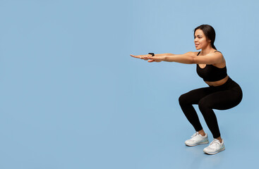 Fototapeta premium Fitness and sport. Slim african american lady in sportswear doing deep squat exercises, working out over blue studio background with empty space. Full length, banner