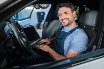 Smiling mechanic running diagnostics using laptop inside car