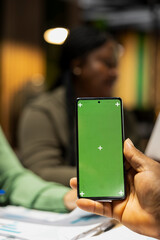 Close up of company CEO holds a phone with isolated mockup, meeting with employees in a late night session. People focusing on company development and making a pitch to obtain funds for a project.