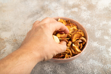 Dried Apples in ceramic bowl with hand on brown concrete. Side view, copy space