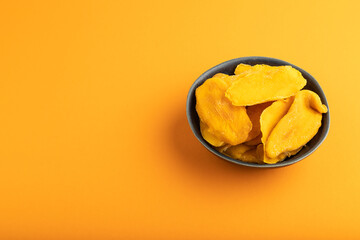 Dried Mango in blue ceramic bowl on orange pastel paper. Side view, copy space