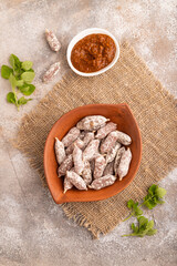Small smoked Chicken sausages in clay bowl on brown concrete. top view, flat lay, close up