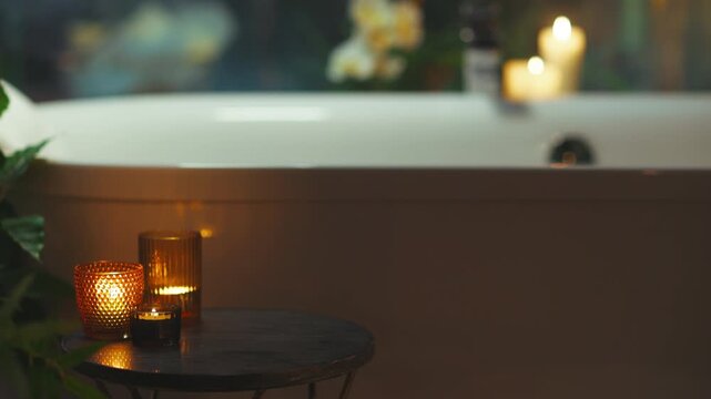 A soothing bathroom scene features a white bathtub in the background and a small, round table in the foreground adorned with three lit candles, casting a warm glow and creating a tranquil, relaxing at