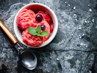 strawberry ice cream with red berries and mint in a white jar seen from above and dark background