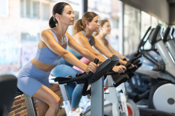 Fototapeta premium Woman in a top and shorts is pedaling an exercise bike. European woman attends group cycling training