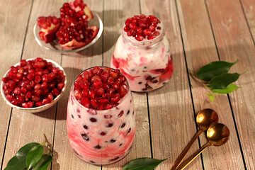 Fruit yogurt with pomegranate seeds and fresh cow cream for healthy nutrition in a glass on an elegant table. Healthy breakfast with ingredients, kitchen background