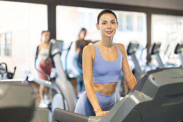 Fototapeta premium Woman in tracksuit at cardio workout, she uses treadmill in gym. European woman doing exercises for body relief