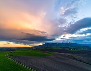 Fototapeta premium Dramatic skyscape over undulating farmlands and distant mountains at twilight hour