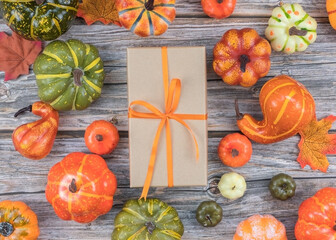 Flatlay autumn gift box with orange ribbon and pumpkins on wood