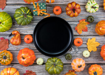 Top view black plate with autumn pumpkins leaves and green gift box on wooden table copy space