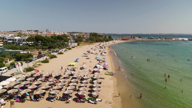 Sandy beach and sea, umbrellas and hotels in Nea Moudania city, Halkidiki, Greece. Aerial panoramic drone view from above, top view from drone. Summer holidays Europe 

