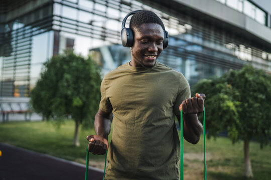 Young sportsman exercising with resistance band listening to music with headphones
