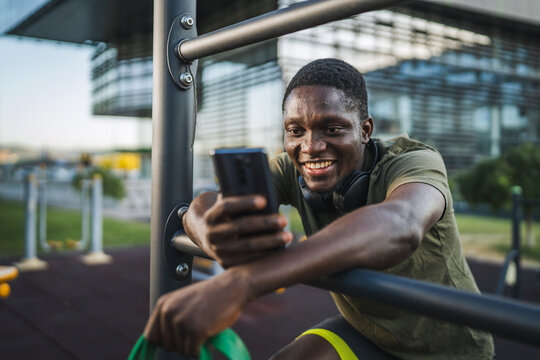 Smiling black man using smart phone at outdoor gym