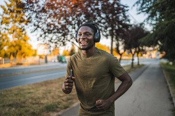 Young man running outdoors while listening to music with headphones and holding a smart phone