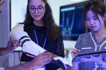 Calibrating a new AI-powered prosthetic. A diverse engineering team witnesses a successful test as the arm's predictive AI flawlessly executes a handshake, based on bio-signal processing data.