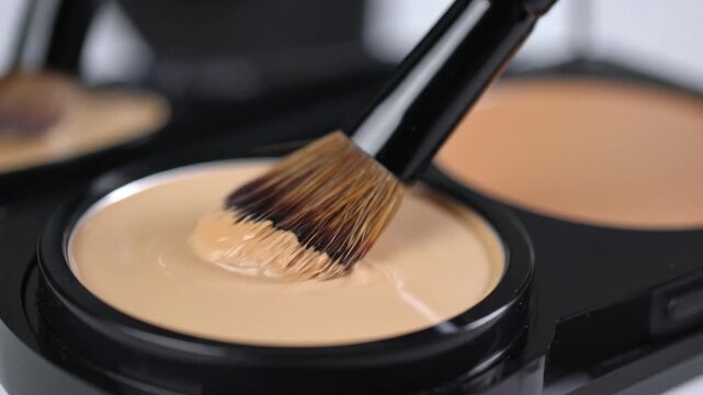 Close Up of Makeup Brush Dipping in Beige Foundation for Cosmetic Application On a Smooth White Surface in Studio Lighting