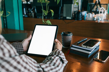 Close-up of hands holding digital tablet with blank screen in cafe, coffee cup and notebooks with smartphone on wooden table
