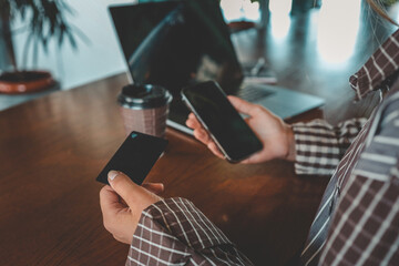 Close-up of hand holding bank card near laptop, coffee cup, and wrapped gift box on cafe table
