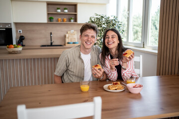 Happy couple enjoying waffles and orange juice for breakfast in modern kitchen