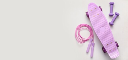 Skateboard , dumbbells and skipping rope on light background with space for text, top view