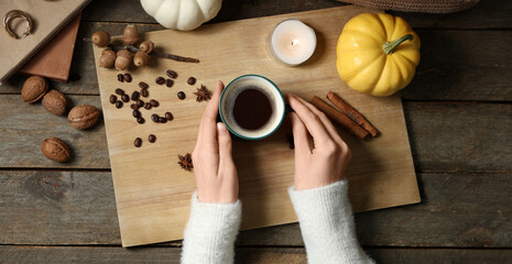 Female hands with cup of tasty pumpkin coffee, autumn decorations, books and warm sweater on brown wooden background, top view