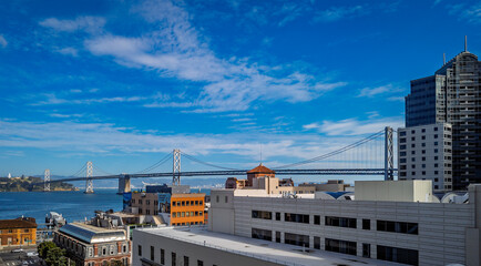 The San Francisco Oakland Bay Bridge spans across the bay with a cityscape and buildings on a clear sunny day in San Francisco, United States