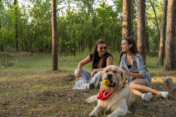 Obraz premium Two girls are walking with retriever dog in the pine forest.