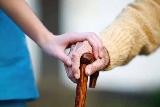 Close up of a young nurse supporting an elderly patient holding a wooden walking stick, offering comfort and care