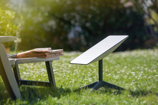 Paris, France - Apr 9, 2025: A Starlink satellite dish is installed in a sunny garden next to a low table holding newspapers, combining cutting-edge connectivity with traditional printed news