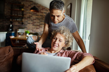 Senior lesbian couple relaxing on sofa using laptop together