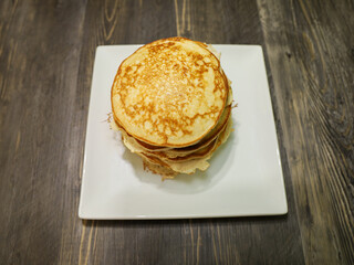 A stack of homemade pancakes without  toppings on a white plate.