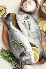 Fresh raw dorado fish, lemon slices, rosemary and spices on white wooden table, flat lay. Organic seafood