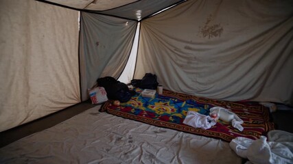 Inside a basic tent setup displaying everyday living conditions in a remote area with scattered belongings
