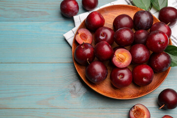 Ripe cherry plums, cloth and green leaves on light blue wooden table, flat lay. Space for text
