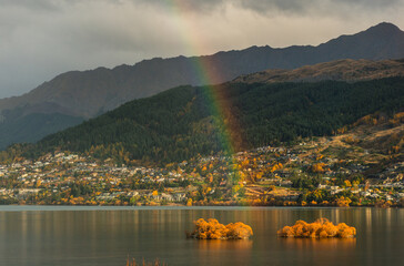 Rainbow over Queenstown lake with many houses and mountains during the autumn time