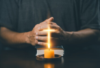 Christian man worship. Hands folded in prayer on a Holy Bible in home concept for faith. Spirituality and religion. Man praying on holy bible with candle light. Man hand with Bible praying.