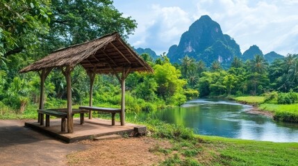 Naklejka premium Rustic wooden gazebo by a river, lush greenery, mountains in background