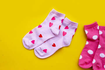 wo pairs of pink socks with heart and polka dot patterns on yellow background
