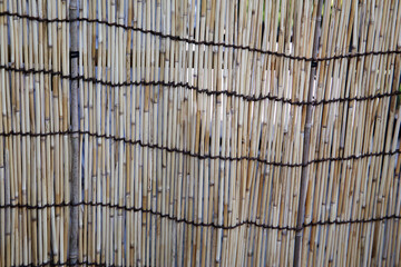 Japanese bamboo fence tied together with dark ropes, creating a natural textured pattern.