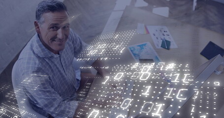 Man wearing plaid shirt typing at desk in office, with printed charts, binary code, copy space