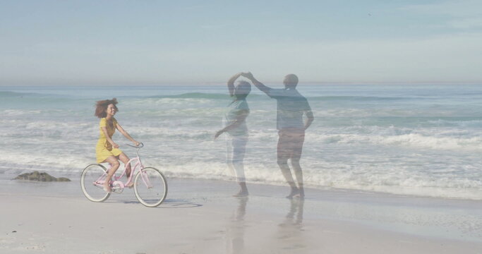 Cycling woman in yellow sundress pedaling pink bicycle at surf beach, with dancing couple reflected - Powered by Adobe