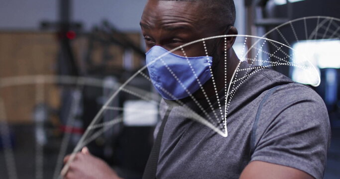 Man wearing gray athletic shirt and medical mask gripping cable handle in gym, with digital overlay - Powered by Adobe