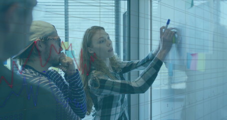 Professionals sketching data on glass board in meeting room, with markers and sticky notes