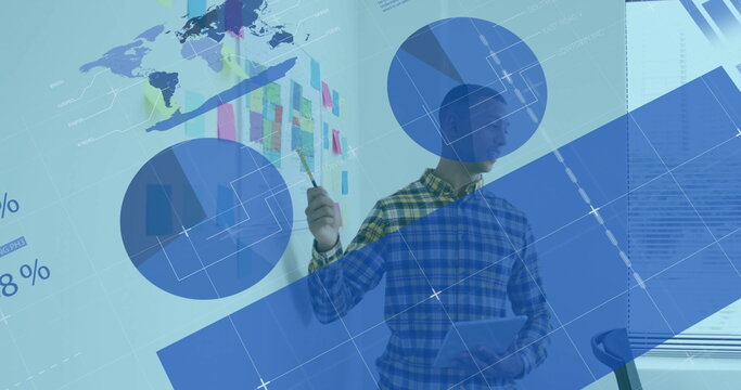 Presenting man wearing checkered shirt gesturing at charts in meeting room, with tablet and pencil