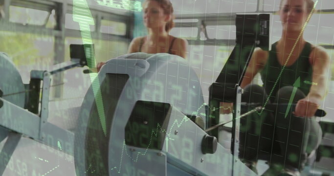 Rowing partners wearing sportswear pulling handles on ergometers at gym, green charts overlay