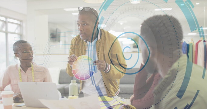 Leaning creative director holding printed color wheel chart around meeting table, with laptop