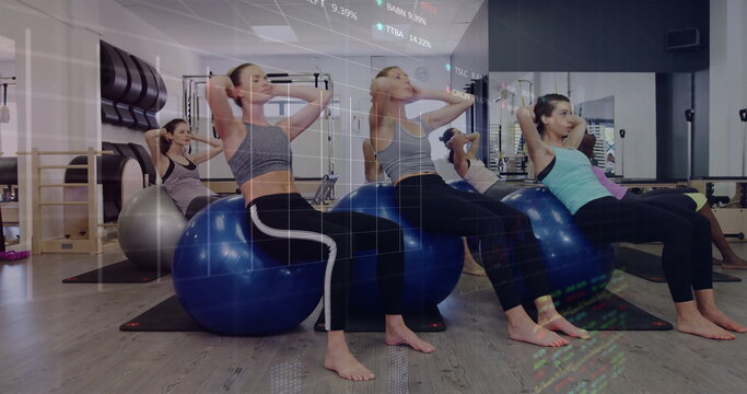 Performing crunches six women balancing on stability balls in fitness studio, with wall bars